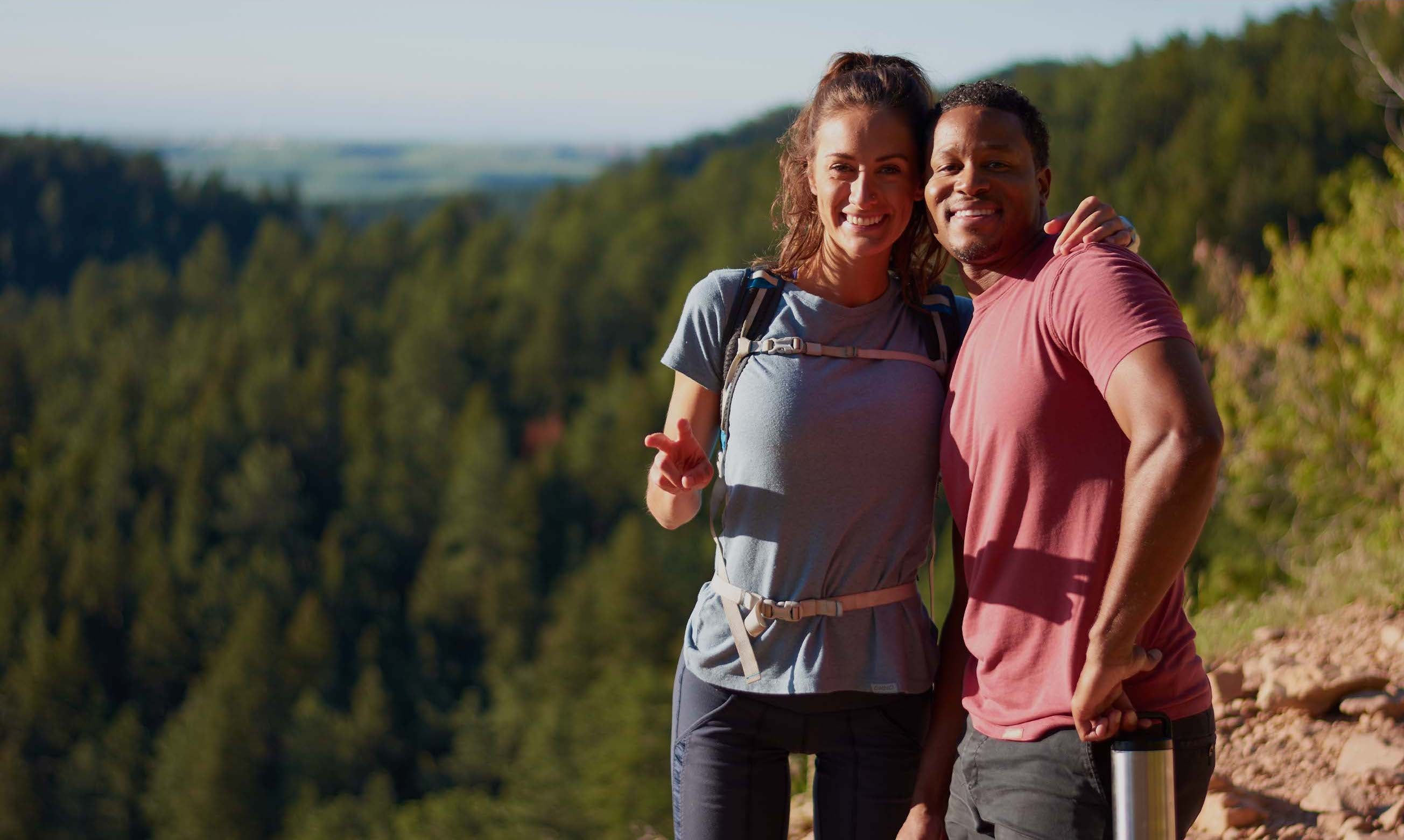 A man and a woman pose for a selfie on a hike, while wearing ONNO t-shirts