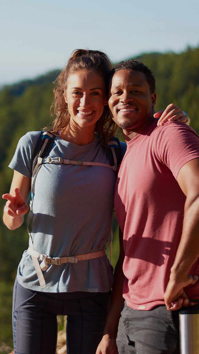A man and a woman pose for a selfie on a hike, while wearing ONNO t-shirts