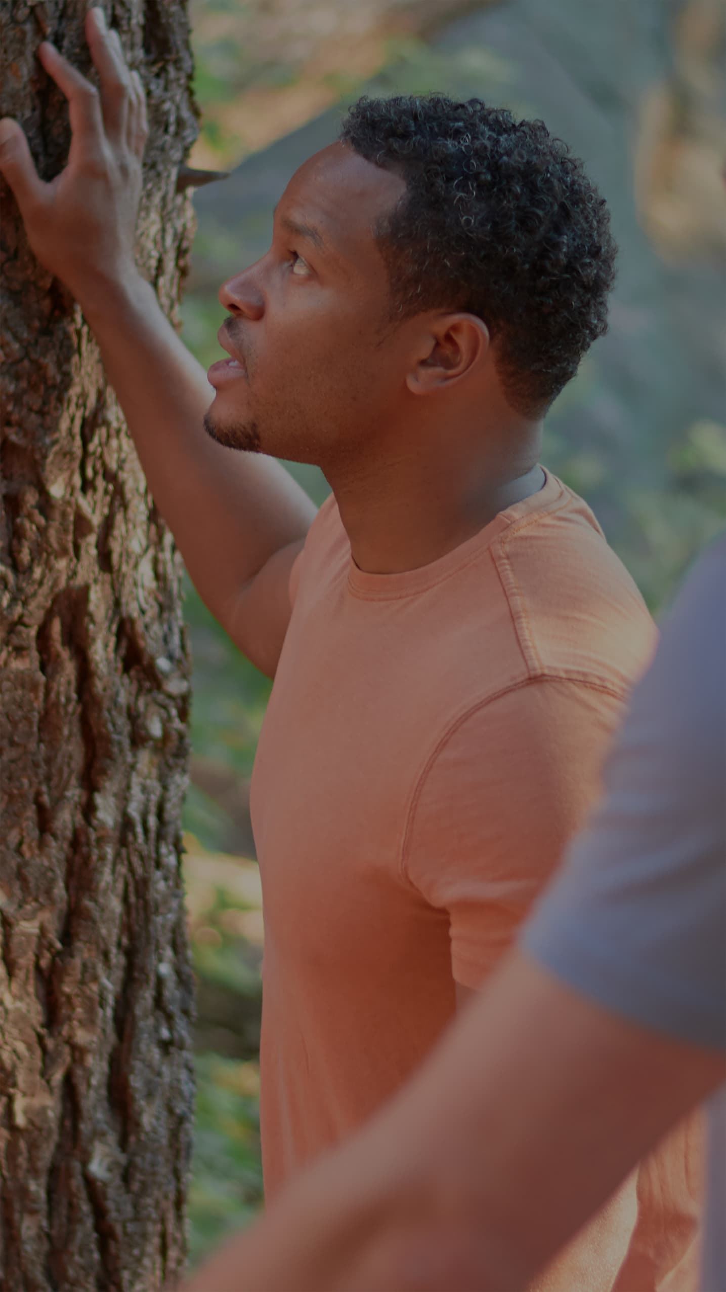 Man in an orange ONNO shirt standing next to a tree