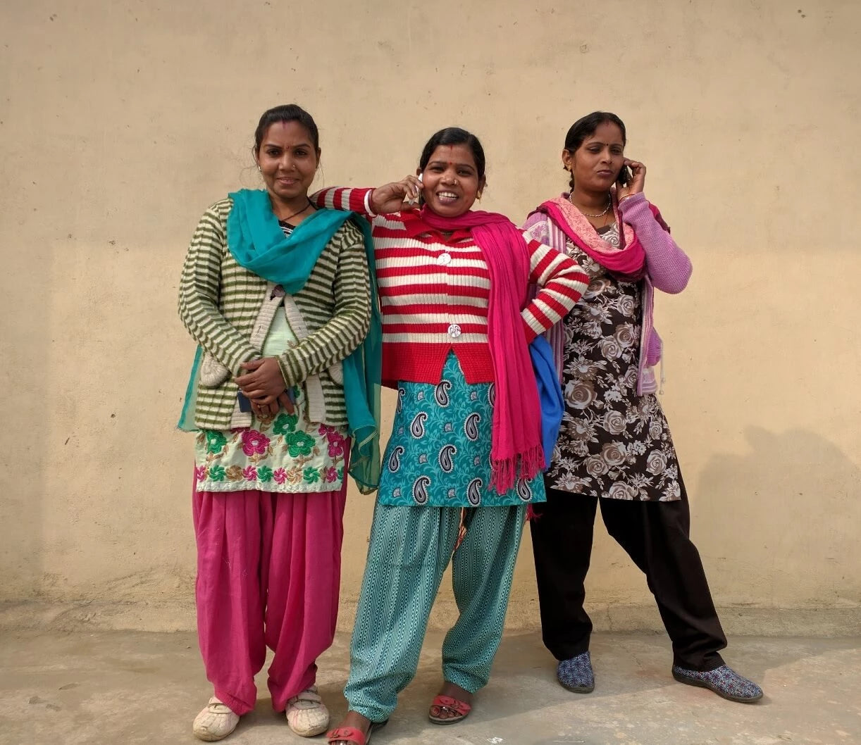 Three Indian women posing for a photo while two make a phone call